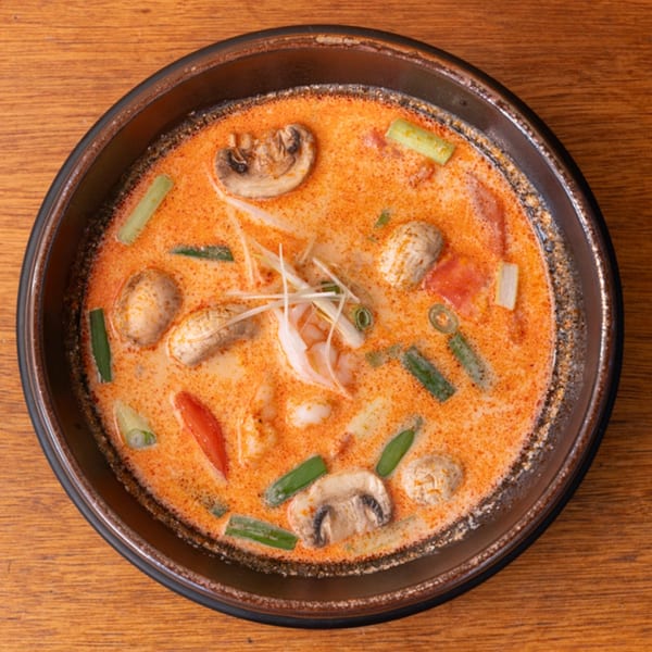 Overhead view of a bowl of Tom Yum soup with shrimp, mushrooms, and green onions.