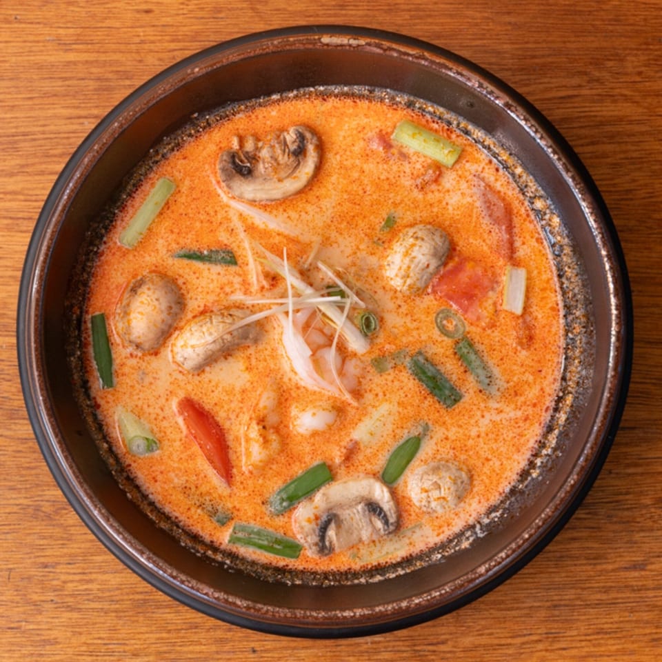 Overhead view of a bowl of Tom Yum soup with shrimp, mushrooms, and green onions.