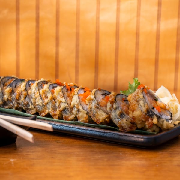 Crispy fried sushi rolls with orange roe, ginger, and lettuce on a black plate with chopsticks.