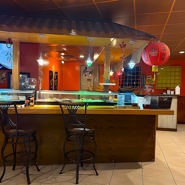 A sushi bar with two stools, red walls, and a large red lantern at Siam Orchid.