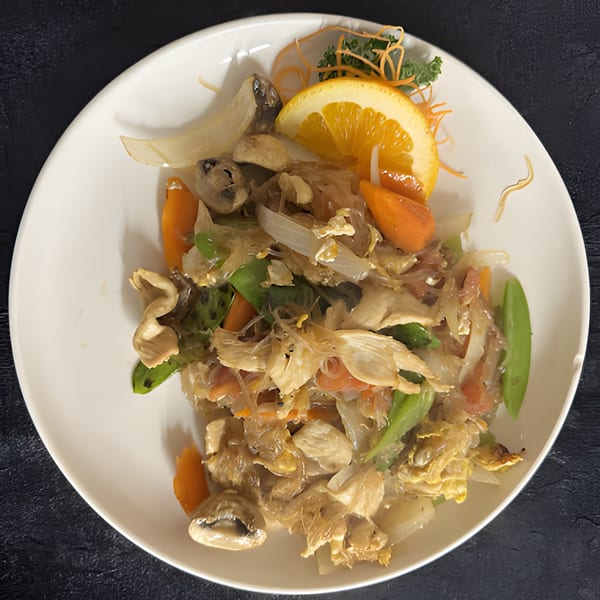 Thai glass noodle stir-fry with chicken, vegetables, and mushrooms, garnished with an orange slice.