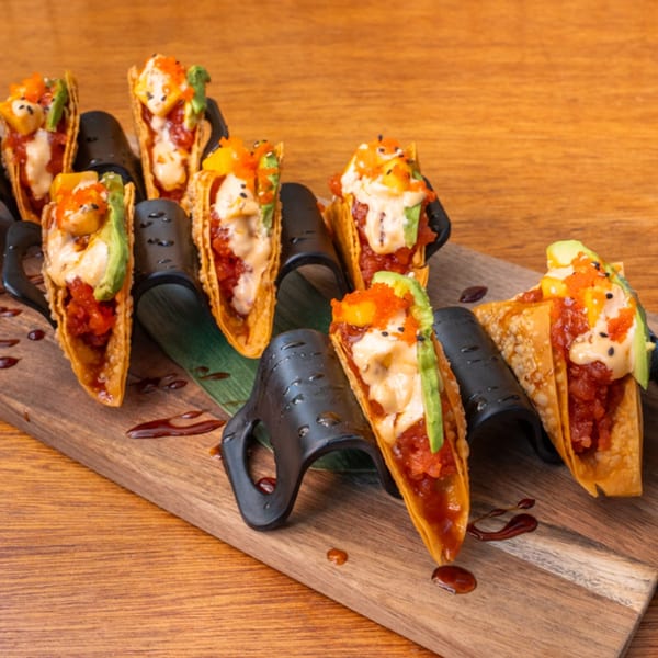 Seven Thai tuna tacos with avocado, mango, and sauce, arranged on a wooden board.