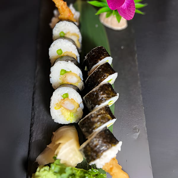 Shrimp tempura sushi rolls with ginger and wasabi on a dark slate plate.