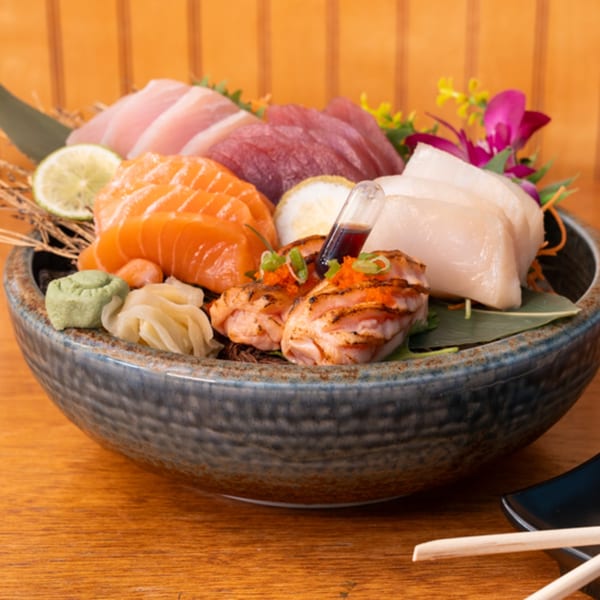 A large bowl of fresh sashimi, including salmon, tuna, and scallops, with wasabi and ginger.