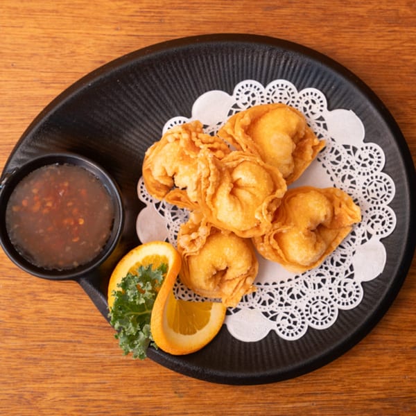 Siam Orchid's golden-fried Thai wontons with sweet chili dipping sauce, orange slice, and kale garnish.