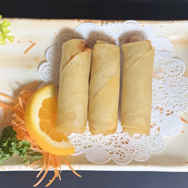 Three golden-brown Thai spring rolls on a white plate with an orange slice and shredded carrots.