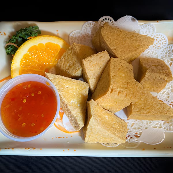 Golden brown fried tofu triangles with sweet chili sauce, orange slice, and greens on a white plate.
